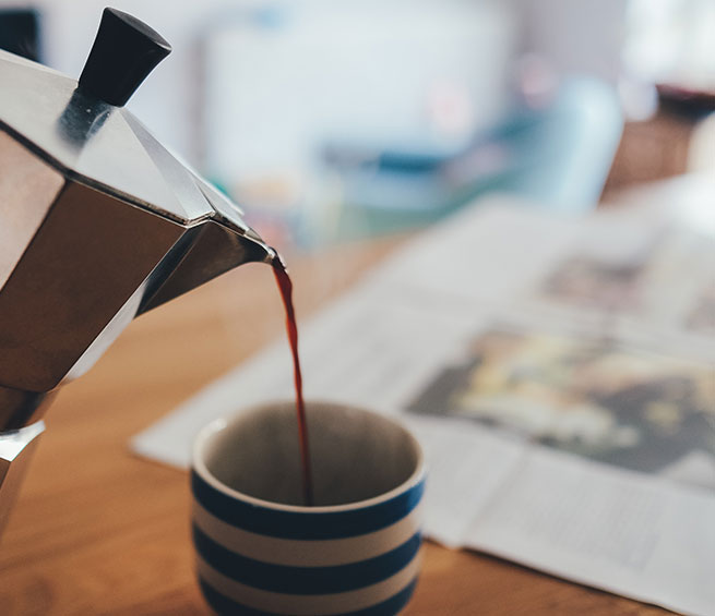 Pouring coffee into a mug with a newspaper and people in the background